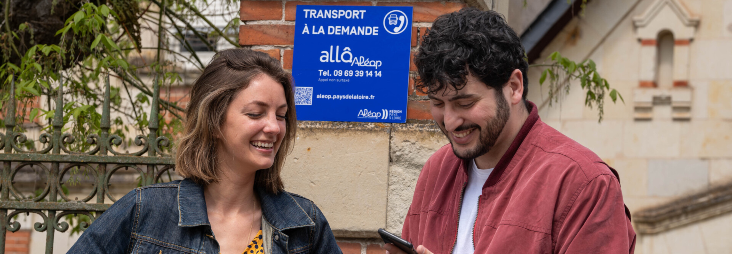 Une femme et un homme consultent un téléphone devant un arrêt du Transport à la demande Région Pays de la Loire